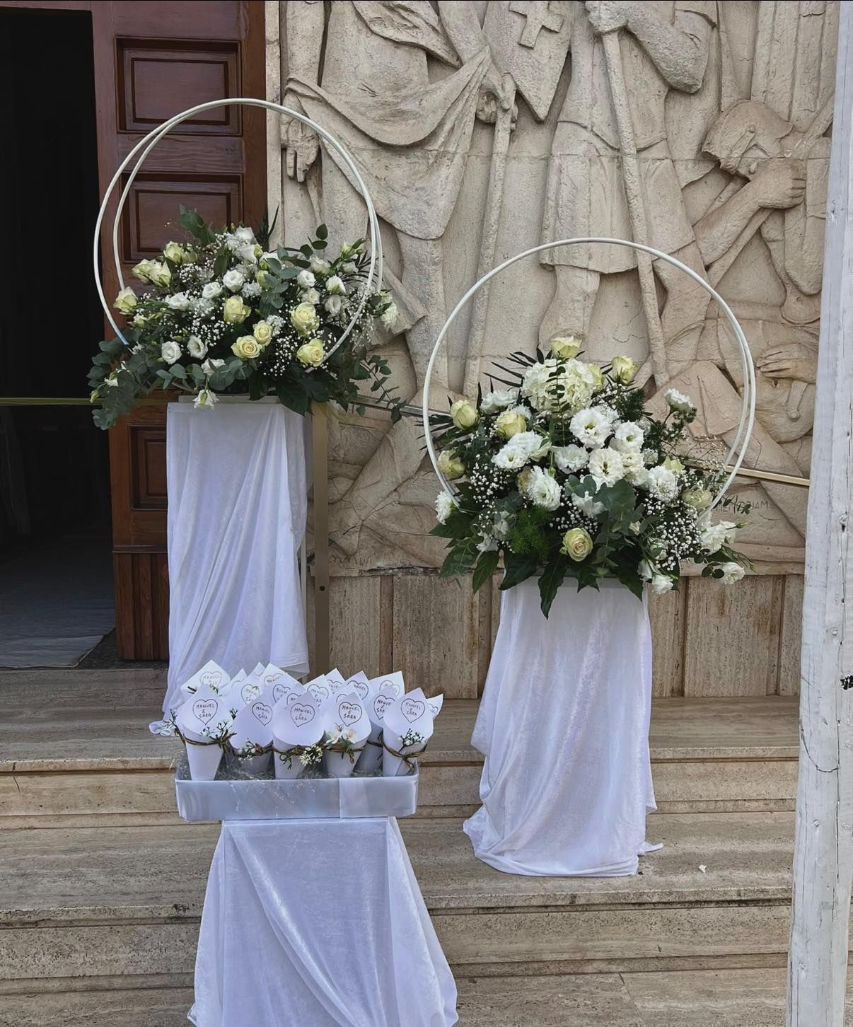 Composizioni floreali con fiori bianchi su piedistalli drappeggiati all'esterno di un edificio.