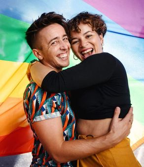 A man and a woman are hugging in front of a rainbow flag.