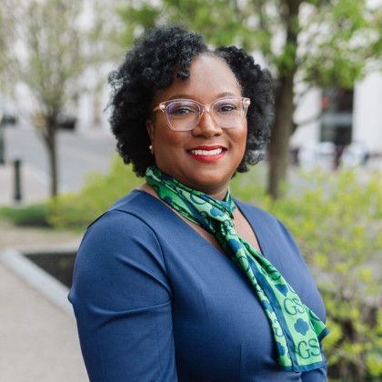 A woman wearing glasses and a green scarf is smiling for the camera.