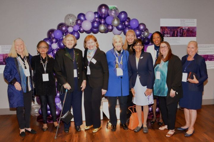 A group of women are posing for a picture in front of purple balloons.