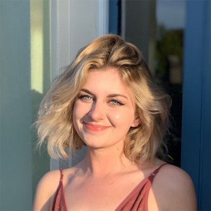 A woman with blonde hair is smiling and standing in front of a blue door.
