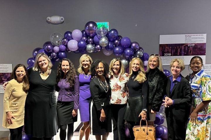 A group of women are posing for a picture in front of a purple balloon arch.