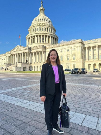 A woman is standing in front of the capitol building holding a purse.