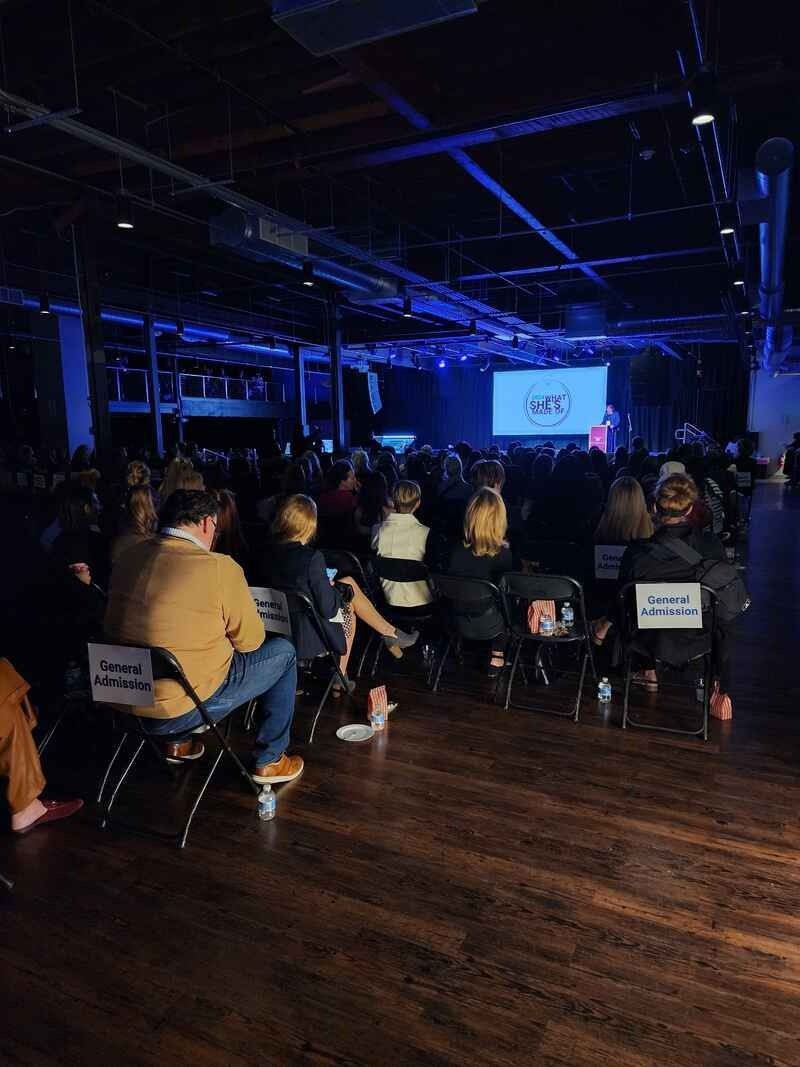 A crowd of people are sitting in chairs in a dark room watching a presentation.