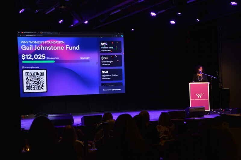 A man stands at a podium in front of a screen that says gall johnstone fund