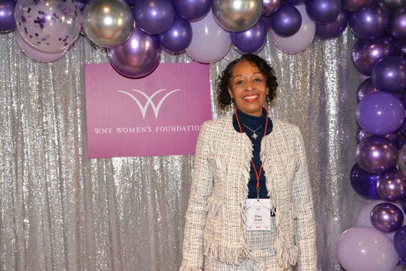 A woman is standing in front of a wall of purple balloons.
