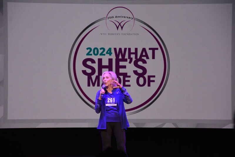 A woman is standing in front of a sign that says 2024 what she 's made of