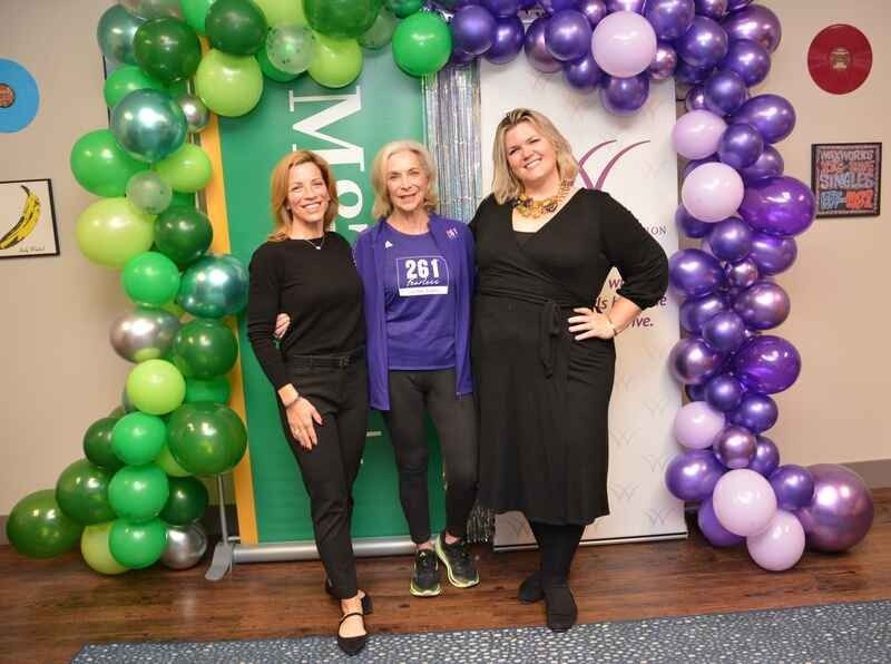 Three women are posing for a picture in front of a balloon arch.