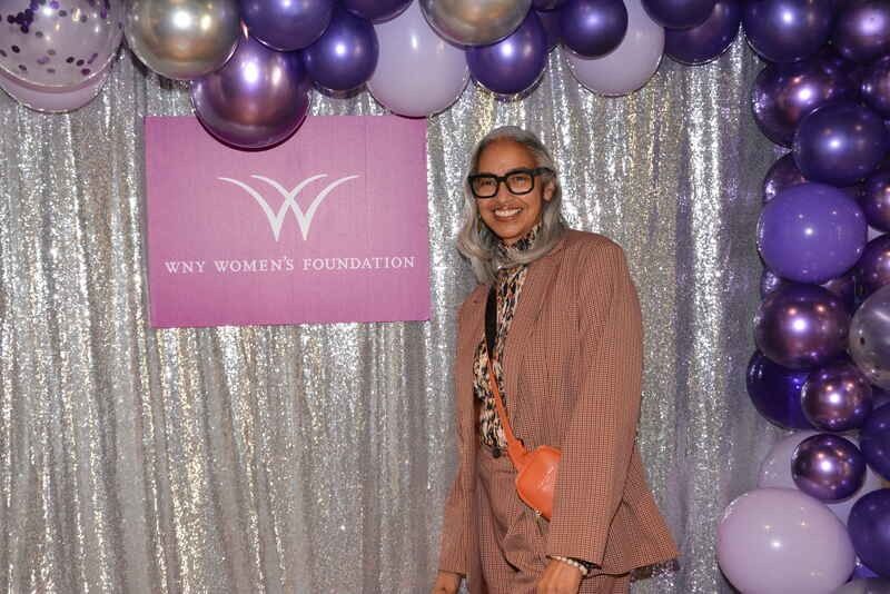 A woman is standing in front of a wall of purple balloons.