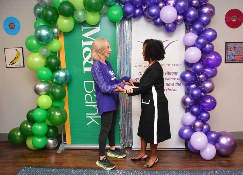 Two women are shaking hands in front of a balloon arch.