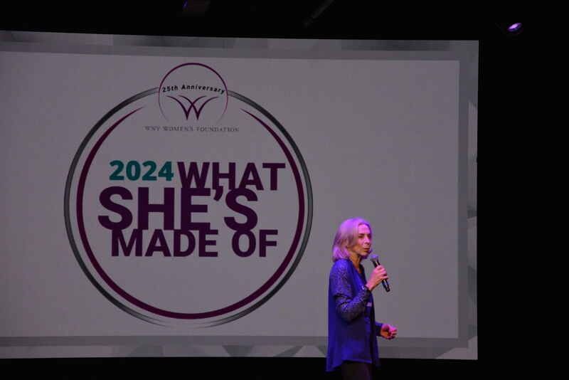 A woman is standing in front of a screen that says `` what she 's made of ''.