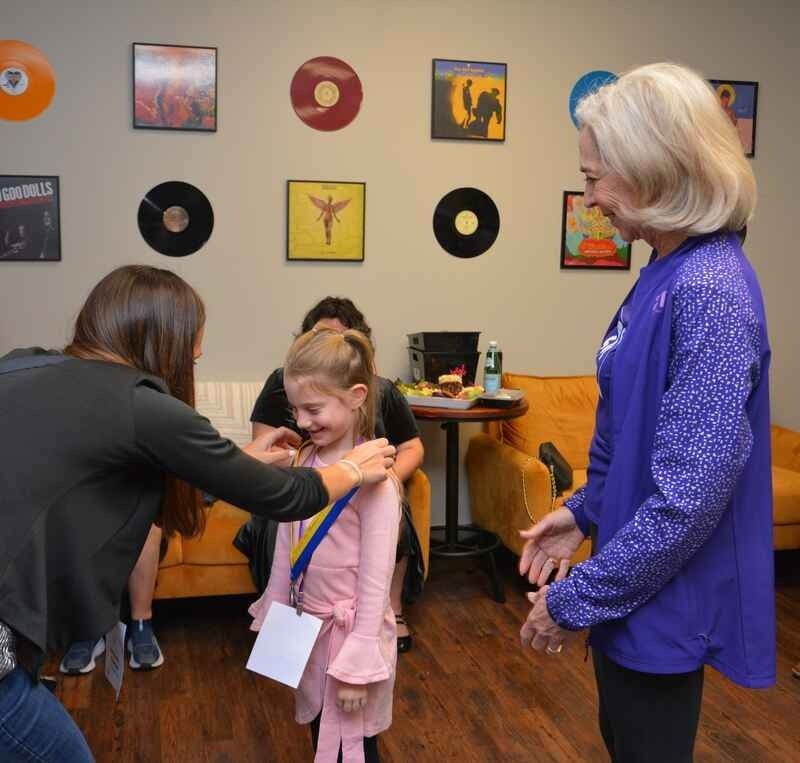 A woman in a purple shirt is putting a medal around a little girl 's neck