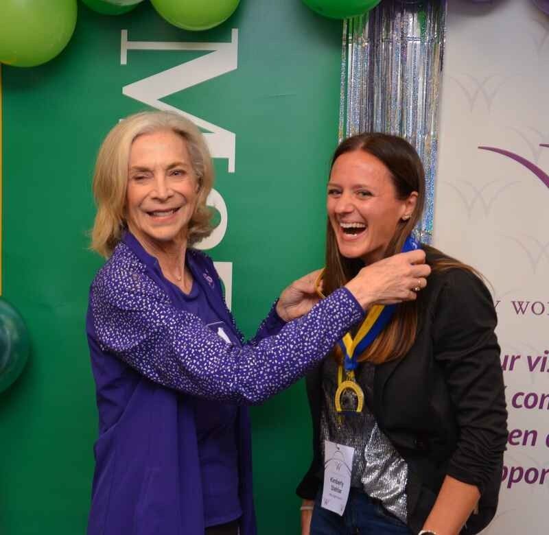 Two women are posing for a picture in front of a sign that says women
