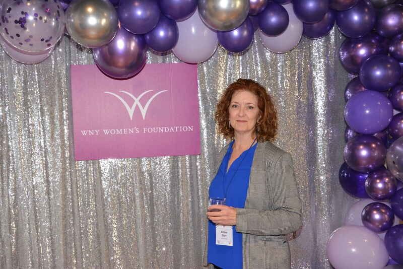 A woman is standing in front of a wall of purple balloons.