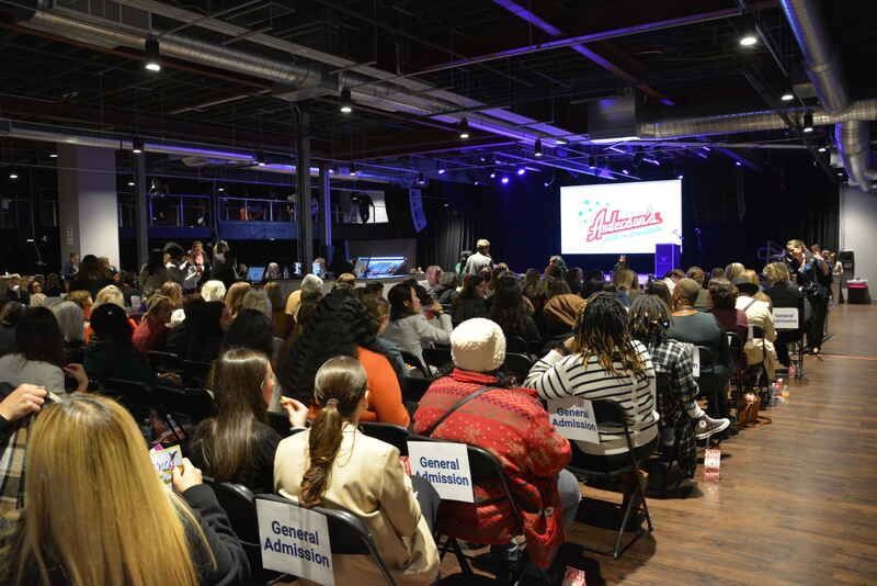 A large group of people are sitting in chairs in front of a stage.