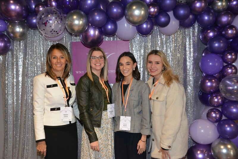 A group of women are posing for a picture in front of purple balloons.