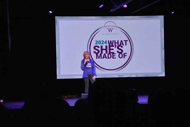 A woman is standing on a stage in front of a screen that says 2024 what she 's made of.