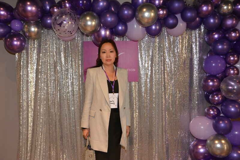 A woman is standing in front of a wall of purple balloons.