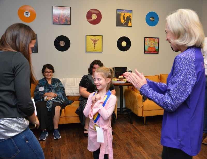A woman in a purple shirt is clapping for a little girl