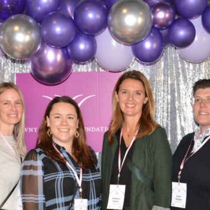 A group of people are posing for a picture in front of purple balloons.