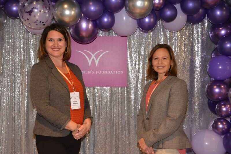 Two women are standing next to each other in front of purple balloons.