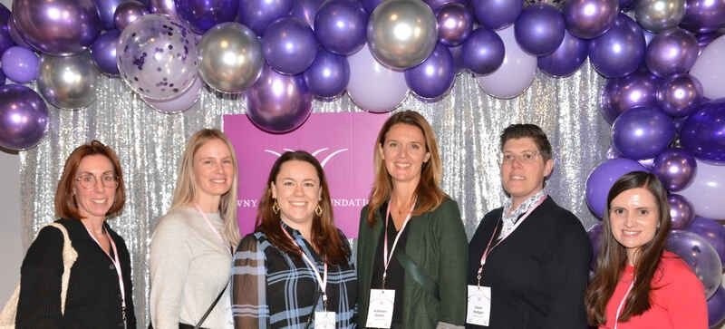A group of people are posing for a picture in front of purple balloons.