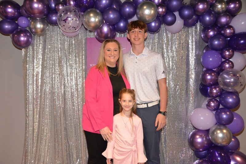A family is posing for a picture in front of purple balloons.