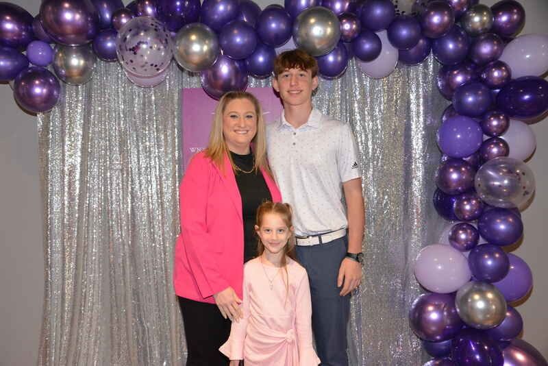 A family is posing for a picture in front of purple balloons.