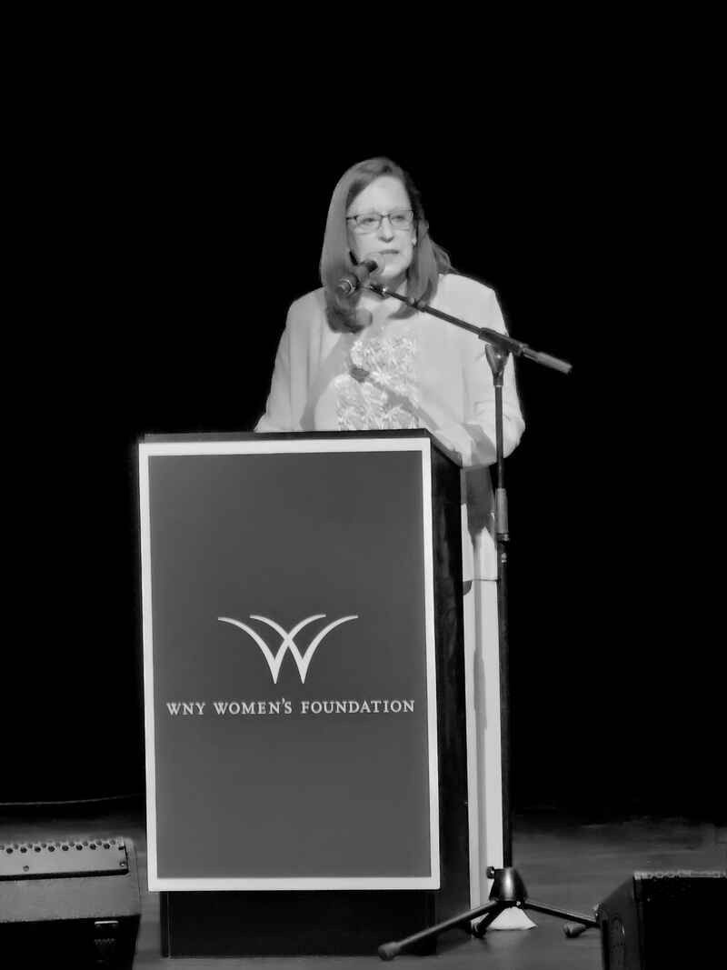 A woman is standing at a podium speaking into a microphone.