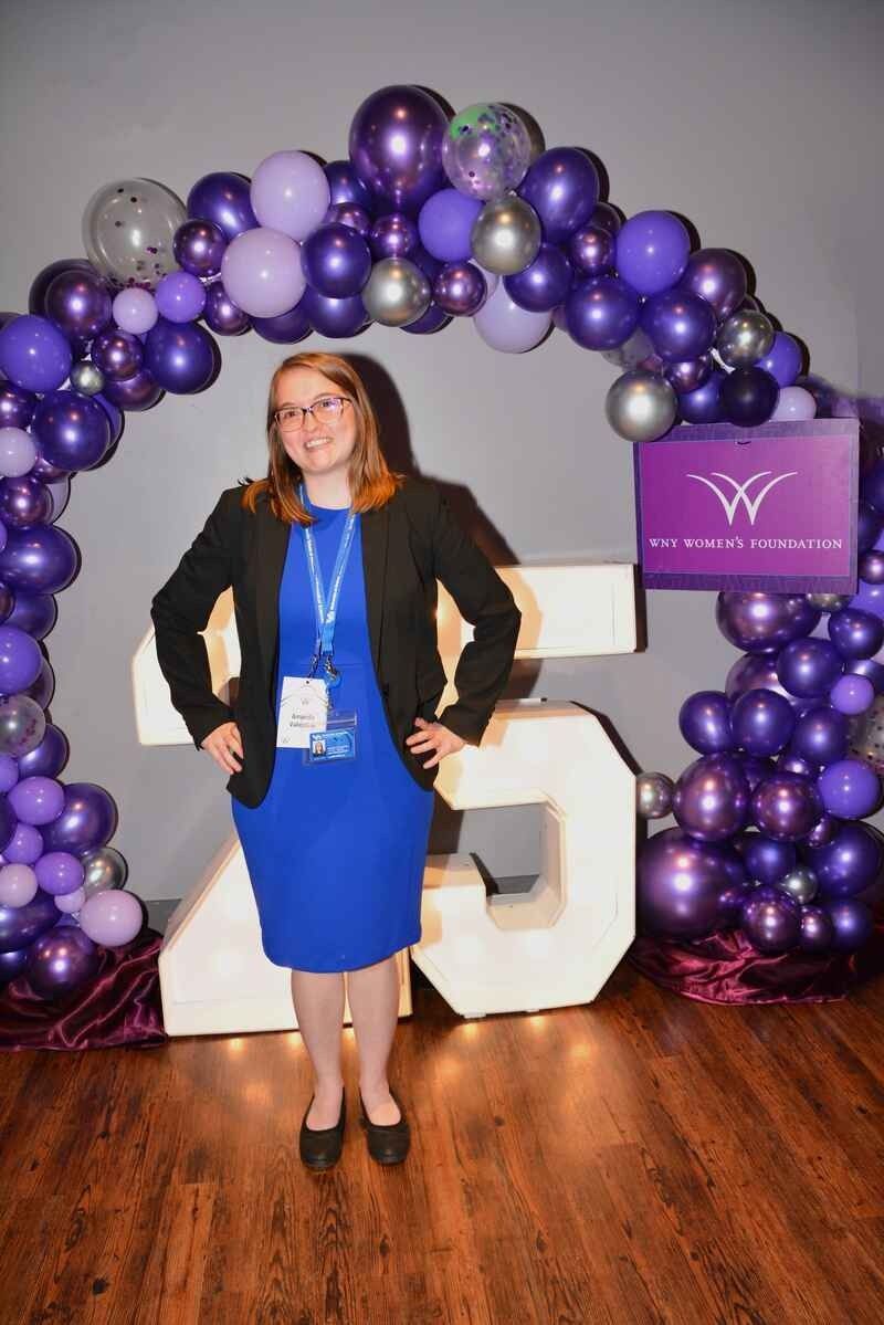 A woman in a blue dress is standing in front of a purple balloon arch.