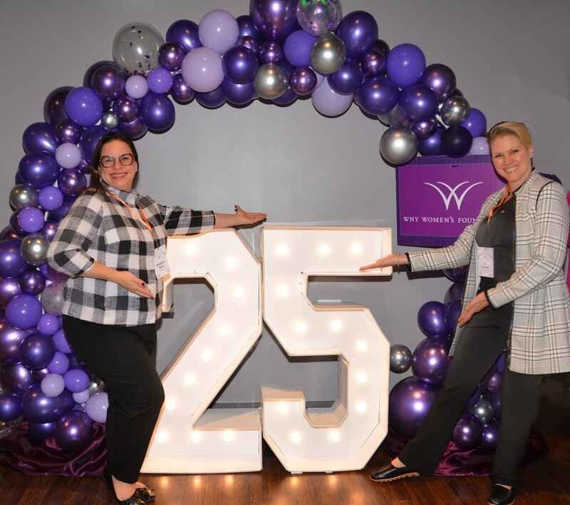 Two women are standing in front of a sign that says 25