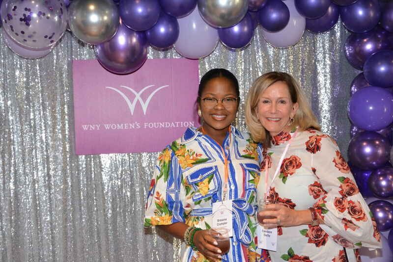 Two women are posing for a picture in front of purple balloons.