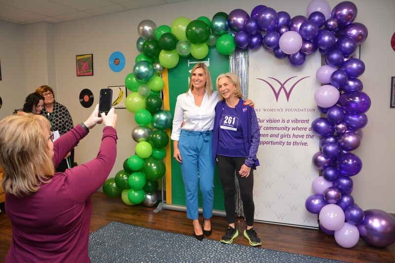 A woman is taking a picture of two women standing in front of balloons.