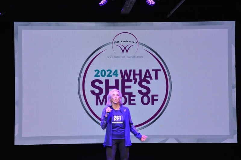A woman is standing in front of a screen that says `` what she 's made of ''.