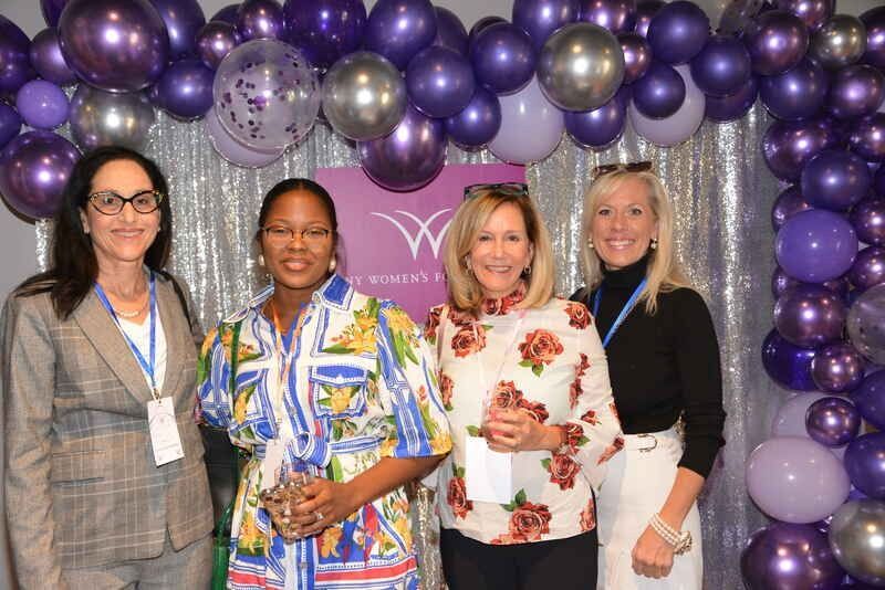 A group of women are posing for a picture in front of purple balloons.