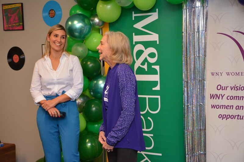 Two women are standing next to each other in front of a m & t bank banner.