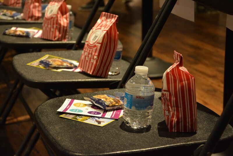 A bottle of water sits on a chair next to a bag of popcorn.