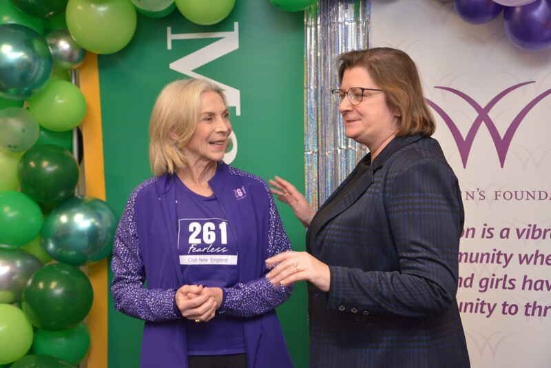 Two women are standing next to each other and one of them is wearing a purple shirt with the number 261 on it.