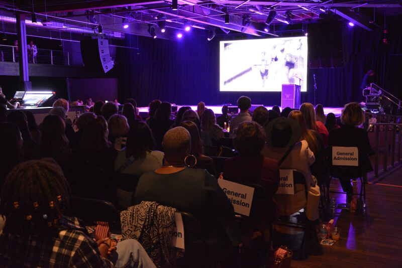 A group of people are sitting in front of a large screen in a dark room.