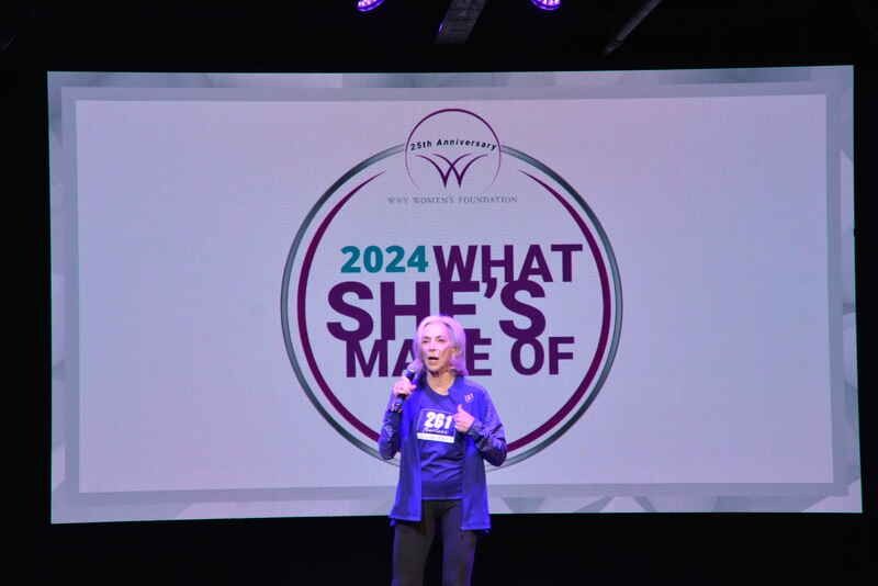 A woman is standing in front of a screen that says 2024 what she 's made of.