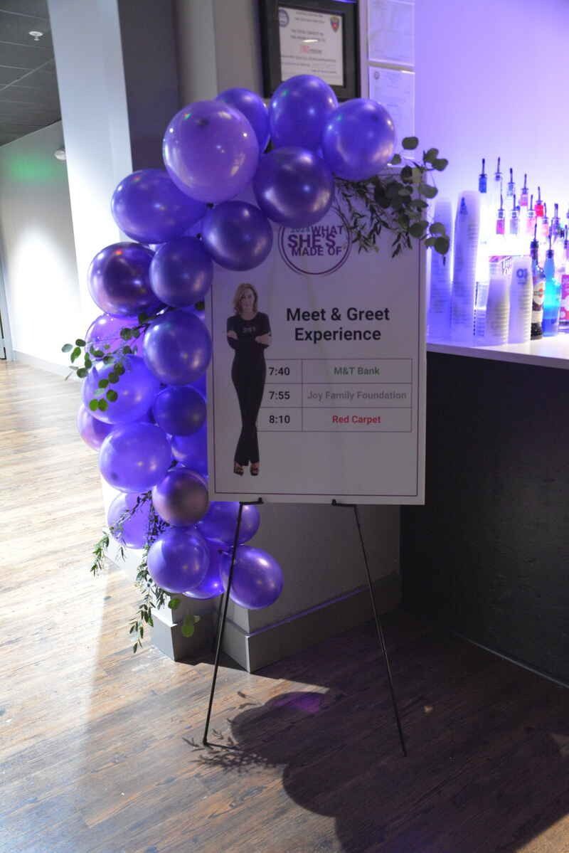 A sign that says meet & greet experience is surrounded by purple balloons