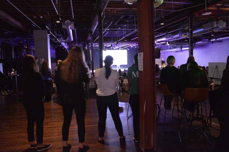 A group of people are standing in a dark room looking at a screen.