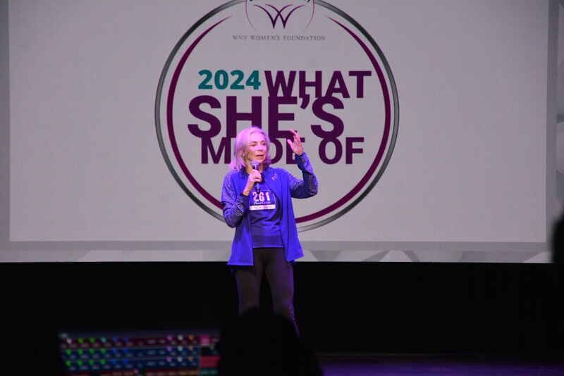 A woman is standing in front of a sign that says 2024 what she 's made of