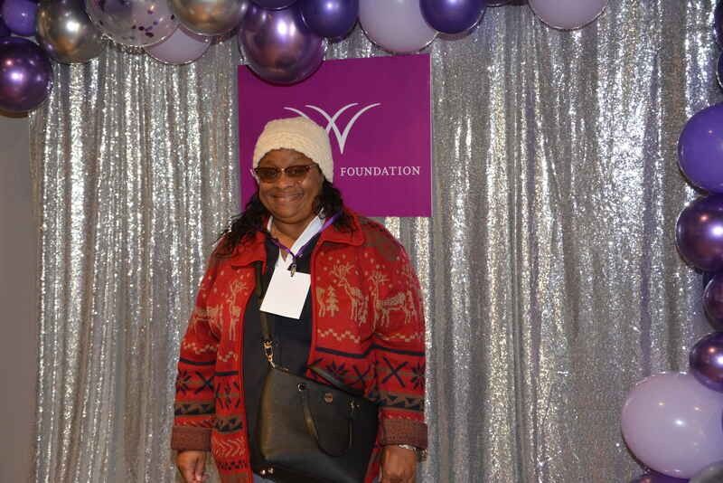 A woman is standing in front of a purple curtain with balloons.