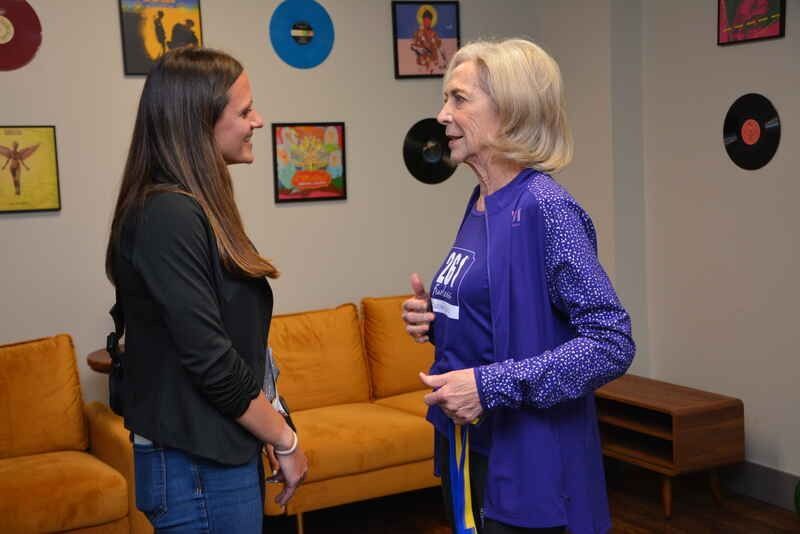Two women are standing next to each other in a living room talking to each other.