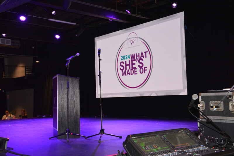 A stage with a projector screen that says what she 's made of