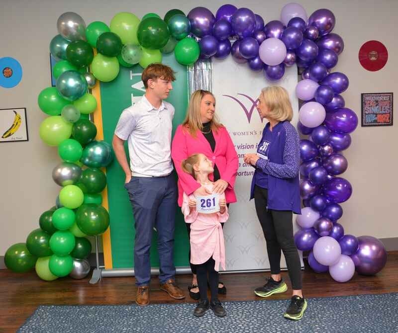 A group of people standing in front of a purple and green balloon arch.