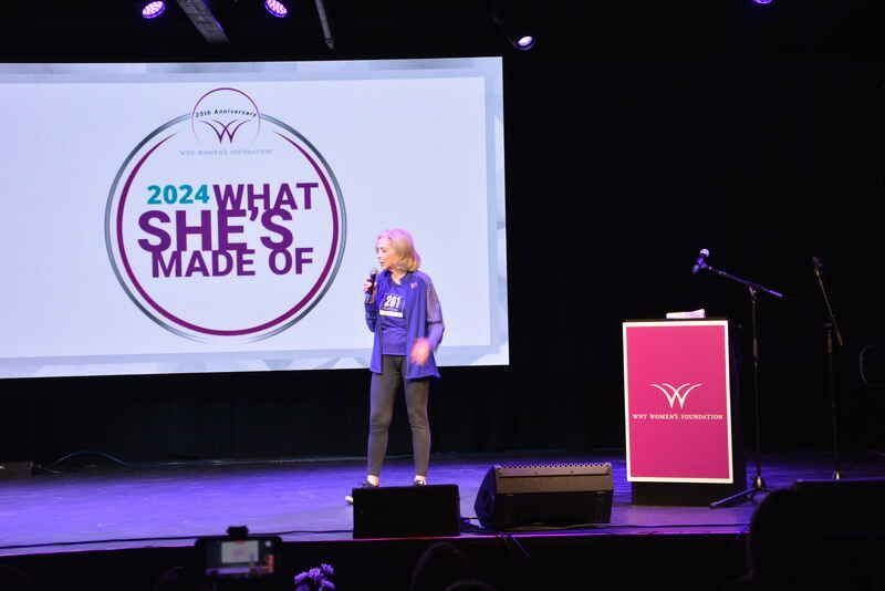 A woman is standing on a stage talking into a microphone.