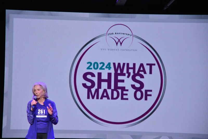 A woman stands in front of a screen that says 2024 what she 's made of