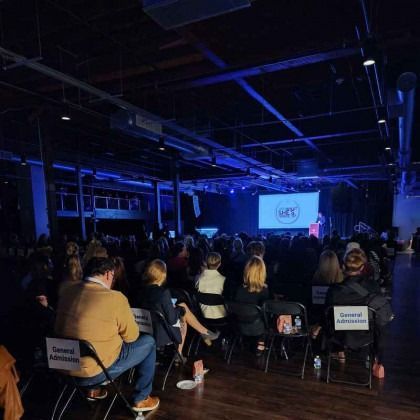 A large group of people are sitting in chairs in front of a stage.